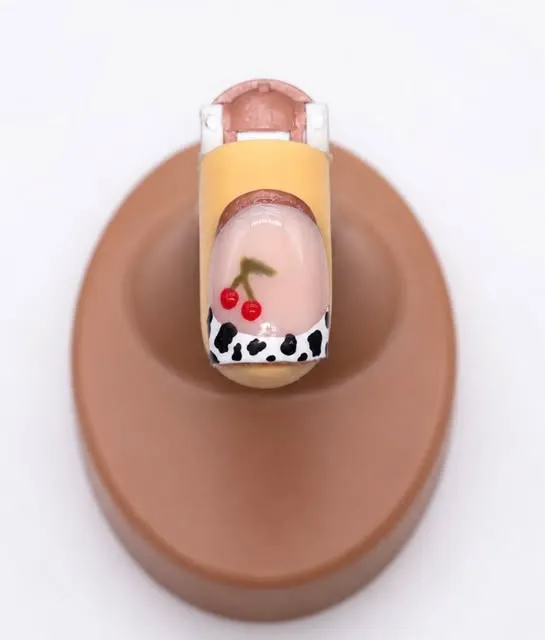 Cherry and cow-print nail art on a practice tip